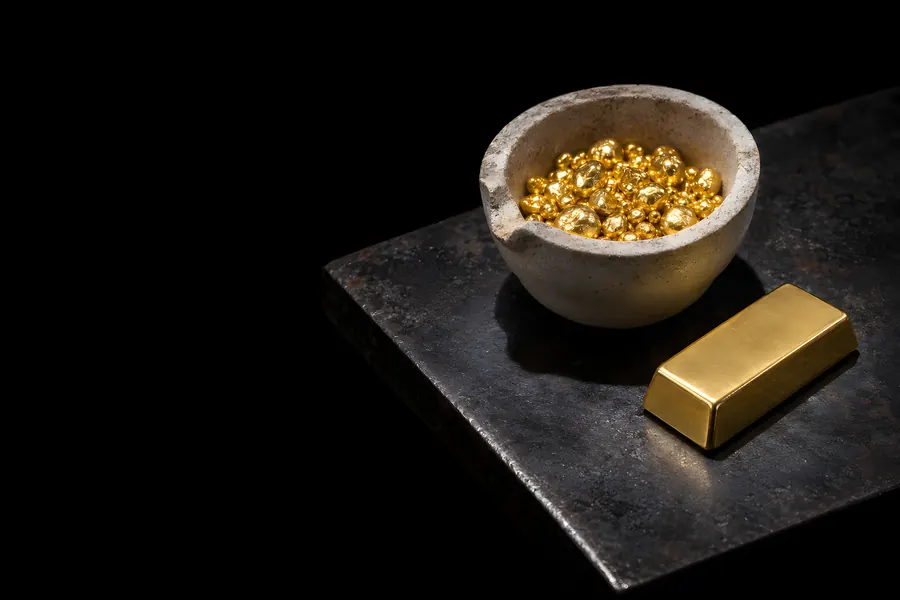 Schmelztiegel mit Goldkörnern und ein kleiner glatter Goldbarren auf einer Stahlplatte